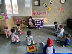 A teacher reads to a group of young children sitting in a circle in a colorful classroom.