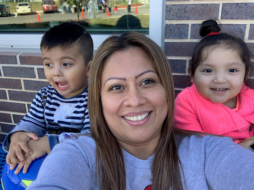 A woman takes a selfie with two smiling children in front of a brick wall.