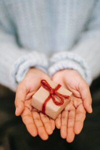 Hands holding a small, brown gift box tied with red string.