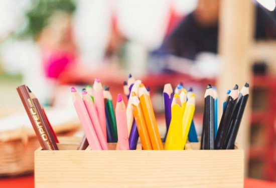 A wooden box holds colorful pencils arranged upright with a blurred background.