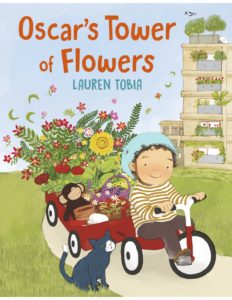 A smiling child rides a tricycle pulling wagons full of flowers, with a cat, monkey toy, and a tall building behind.