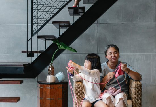 Woman and girl knitting on a chair while another child climbs stairs in a modern home.