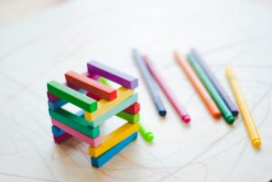 Colorful wooden blocks stacked in a square and colored pencils scattered on a white surface.