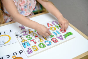Child placing colorful alphabet puzzle pieces on a white table, with flashcards nearby.