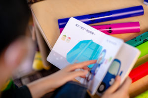 A child reads a colorful picture book with Chinese text at a table with colorful tubes.