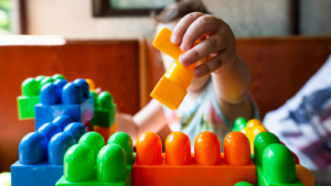 A child playing with colorful plastic building blocks, holding up a yellow piece.