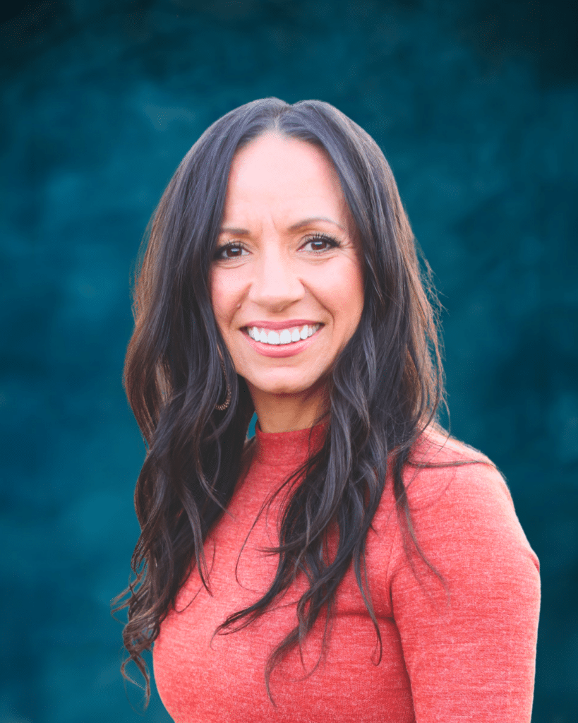 Woman with long dark hair wearing an orange top, smiling in front of a blue textured background.